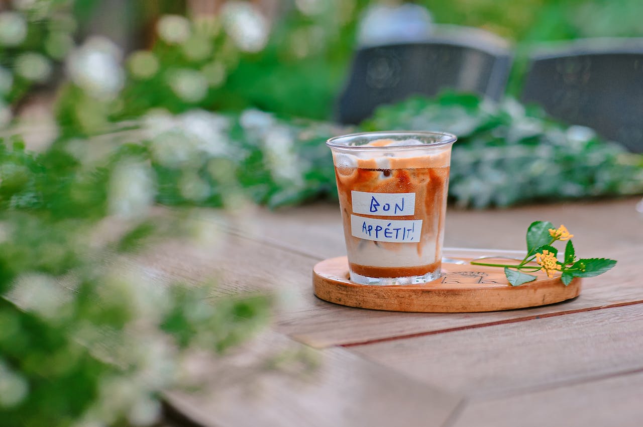services-03 Close-up of an iced coffee with a Bon Appétit note on a wooden table outdoors.